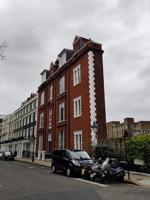 A row of classic Victorian-style terraced townhouses with cream and beige facades and decorative white mouldings along a busy London street, with several pedestrians walking on the sidewalk and a pers